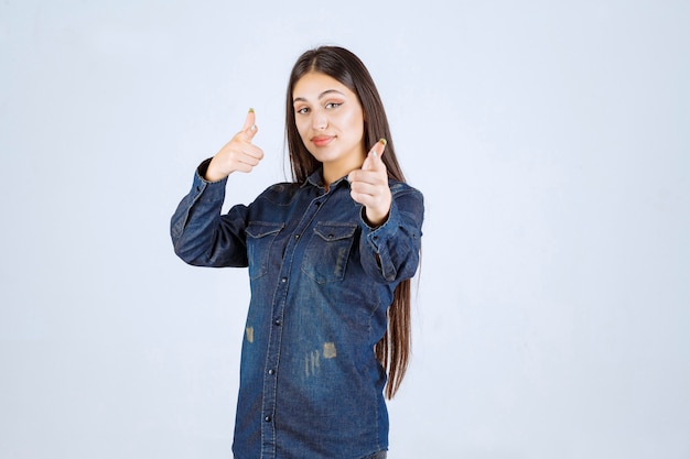 Junge Frau im Jeanshemd, die jemanden nach vorne zeigt und ihn einlädt