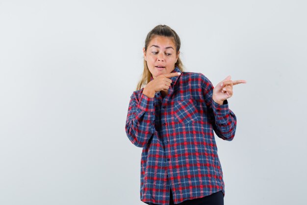 Junge Frau im karierten Hemd, das mit Zeigefingern rechts zeigt und glücklich schaut