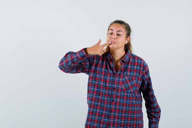 Junge Frau im karierten Hemd, das Zeigefinger auf Mund setzt und ernst schaut