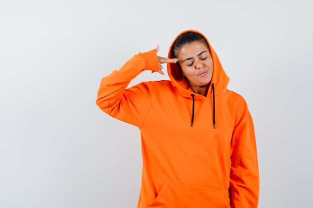 Junge Frau im orangefarbenen Hoodie, die mit dem Zeigefinger auf sich selbst zeigt und ernst aussieht