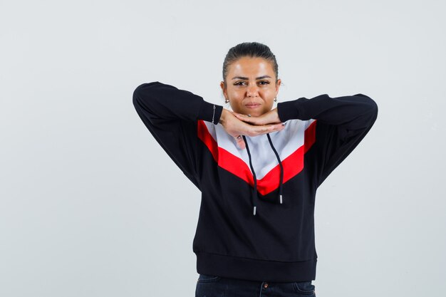 Junge Frau im Pullover und in den schwarzen Jeans, die Hände unter Kinn setzen und hübsch, Vorderansicht schauen.