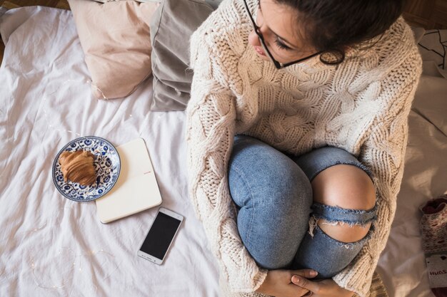 Junge Frau im Pullover und in Jeans, die auf Bett sitzen