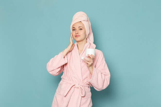 junge Frau im rosa Bademantel nach dem Duschen mit Creme auf Blau