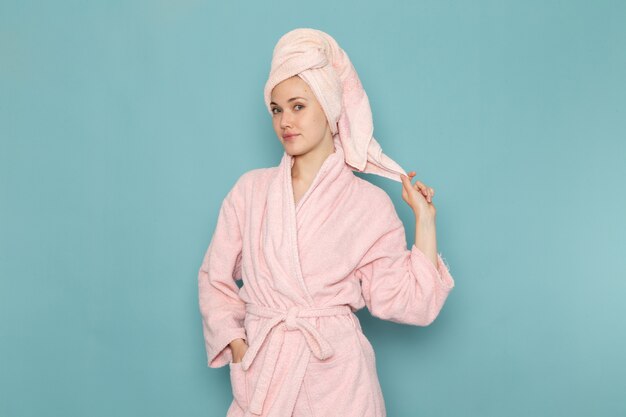 junge Frau im rosa Bademantel nach der Dusche, die lächelnd auf Blau aufwirft