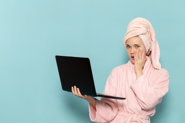 junge Frau im rosa Bademantel nach der Dusche mit Laptop auf blau