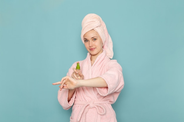 junge Frau im rosa Bademantel nach der Dusche mit Spray auf blau