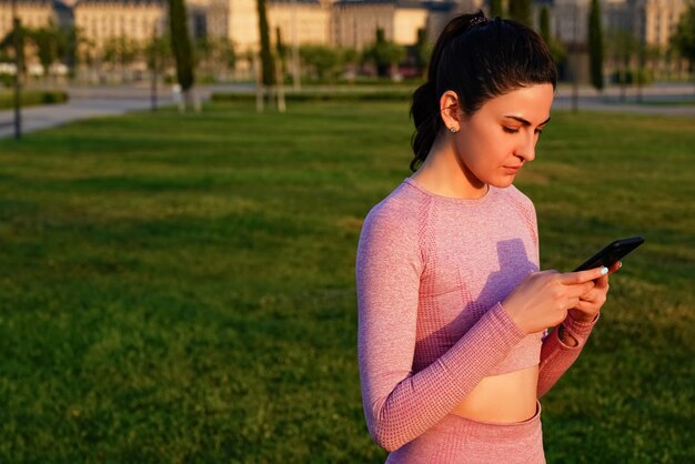 junge Frau im rosa Hemd mit ihrem Telefon im Park um Gras tagsüber