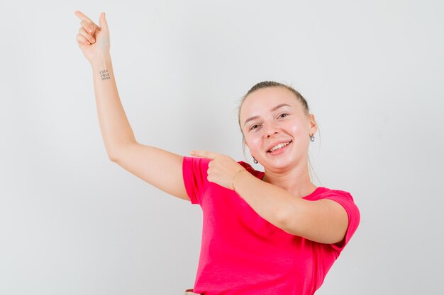 Junge Frau im rosa T-Shirt zeigt auf die obere linke Ecke und sieht froh aus