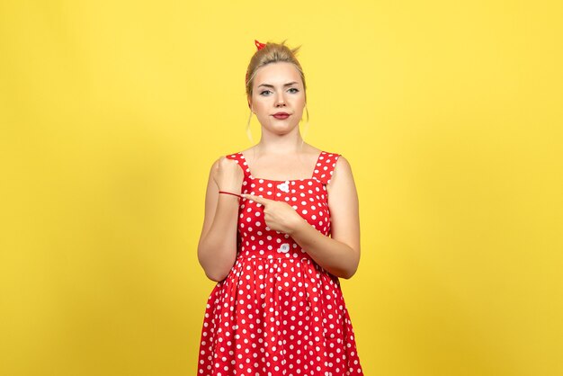 junge Frau im roten gepunkteten Kleid, das ihr Handgelenk auf gelb zeigt