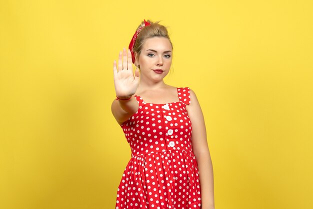 junge Frau im roten gepunkteten Kleid, das Stoppschild auf Gelb zeigt