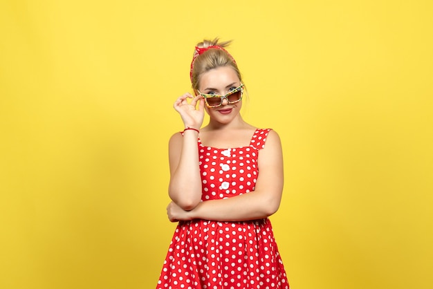 junge Frau im roten gepunkteten Kleid mit Sonnenbrille, die auf Gelb aufwirft