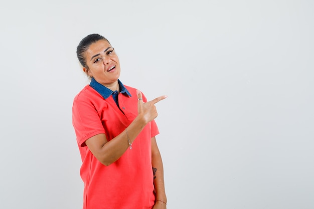 Junge Frau im roten Hemd, das mit Zeigefinger nach rechts zeigt und hübsch aussieht, Vorderansicht.