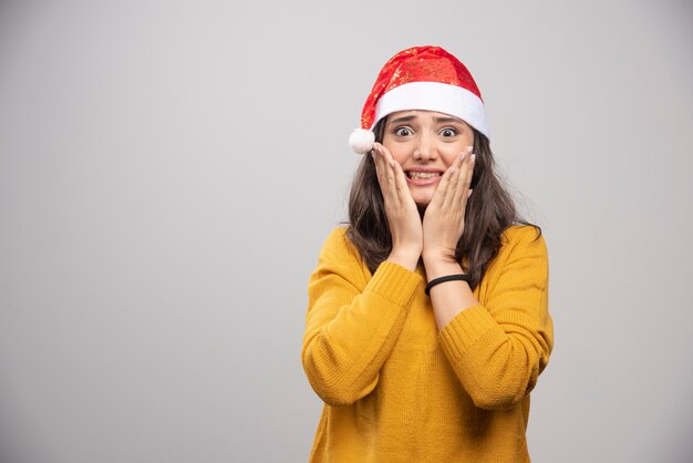 Junge Frau im roten Hut des Weihnachtsmanns, der über einer weißen Wand aufwirft.