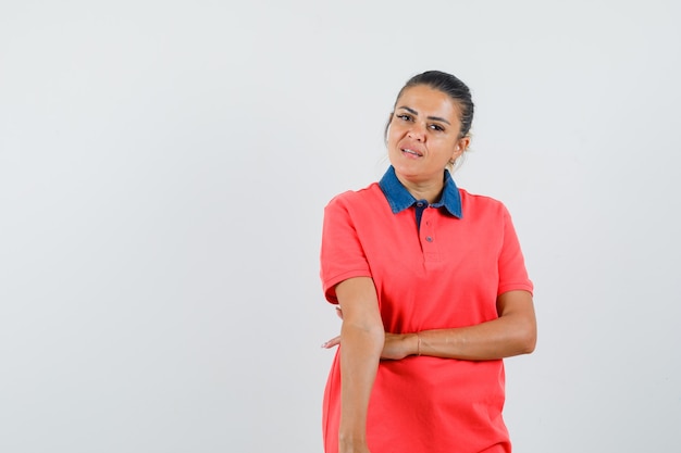 Junge Frau im roten T-Shirt, das Arme streckt und hübsch, Vorderansicht schaut.