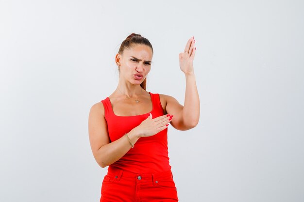 Junge Frau im roten Trägershirt, Hosen, die Karate-Hieb-Geste zeigen und zuversichtlich, Vorderansicht schauen.