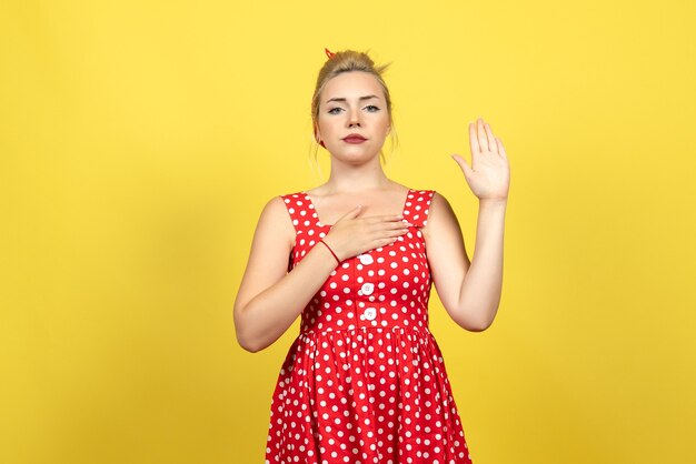junge Frau im roten Tupfenkleid, das emotional ihre eine Hand auf Gelb erhebt