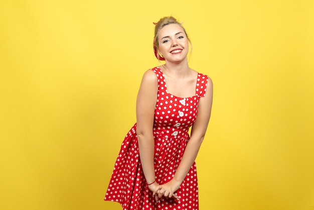 junge Frau im roten Tupfenkleid, das glücklich auf Gelb aufwirft
