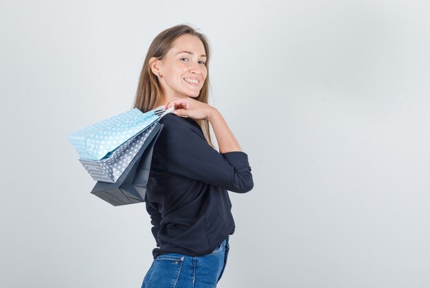 Junge Frau im schwarzen Hemd, Jeansshorts, die Papiertüten halten und fröhlich schauen