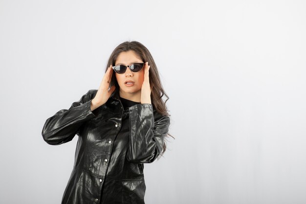 junge Frau im schwarzen Mantel mit Brille und posiert.