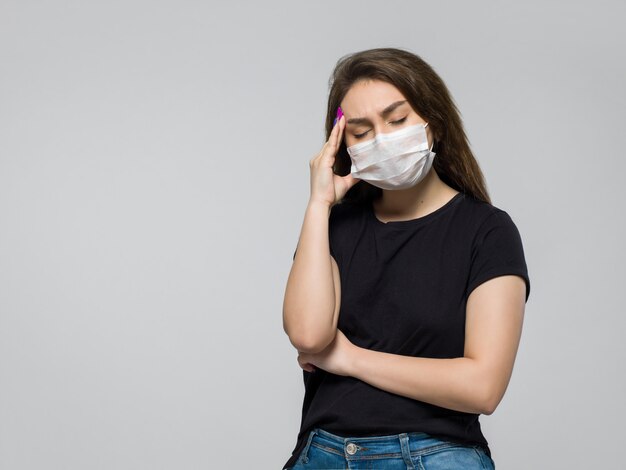 Junge Frau im schwarzen T-Shirt und in der weißen sterilen medizinischen Maske mit starken Kopfschmerzen