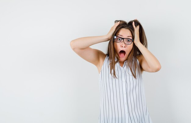 Junge Frau im T-Shirt, das Finger im Haar hält und verrückt schaut, Vorderansicht.