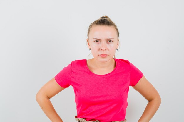 Junge Frau im T-Shirt, das Hände auf Taille hält und verdächtig schaut