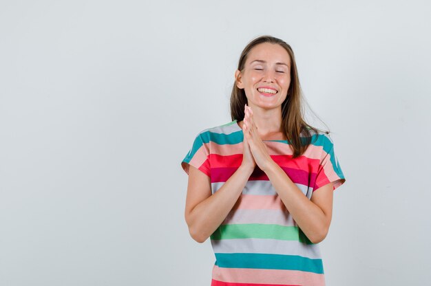 Junge Frau im T-Shirt, das Hände zusammenhält und hoffnungsvoll, Vorderansicht schaut.