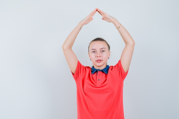 Junge Frau im T-Shirt, das Hausdachzeichen über Kopf macht