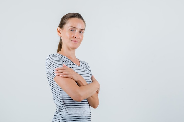 Junge Frau im T-Shirt, das mit verschränkten Armen steht und fröhlich, Vorderansicht schaut.