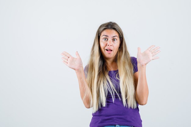 Junge Frau im T-Shirt, das offene Handflächen zeigt und fröhlich, Vorderansicht schaut.