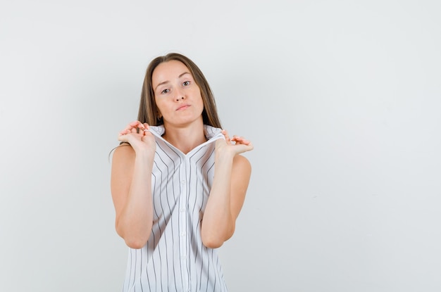 Junge Frau im T-Shirt hält Kragen und schaut ernst, Vorderansicht.