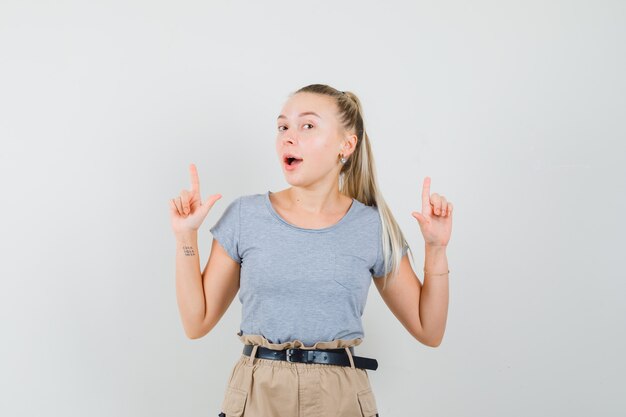 Junge Frau im T-Shirt, Hose zeigt nach oben und schaut freudig, Vorderansicht.