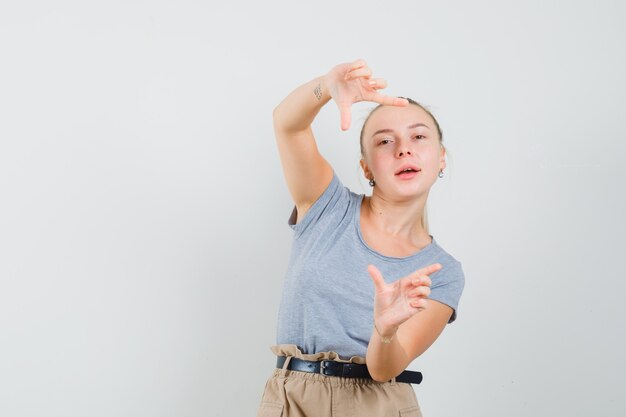 Junge Frau im T-Shirt, Hosen, die Rahmengeste machen und munter aussehen, Vorderansicht.