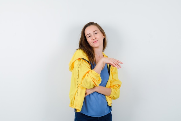 Junge Frau im T-Shirt, Jacke, die im Stehen aufwirft und entzückend aussieht, Vorderansicht.