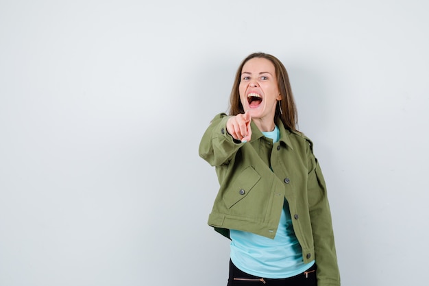 Junge Frau im T-Shirt, Jacke, die nach vorne zeigt und energisch aussieht, Vorderansicht.