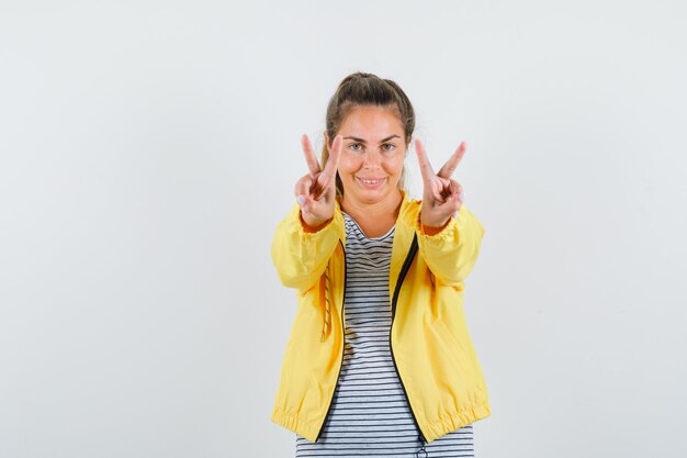 Junge Frau im T-Shirt, Jacke, die Siegesgeste zeigt und glücklich schaut, Vorderansicht.