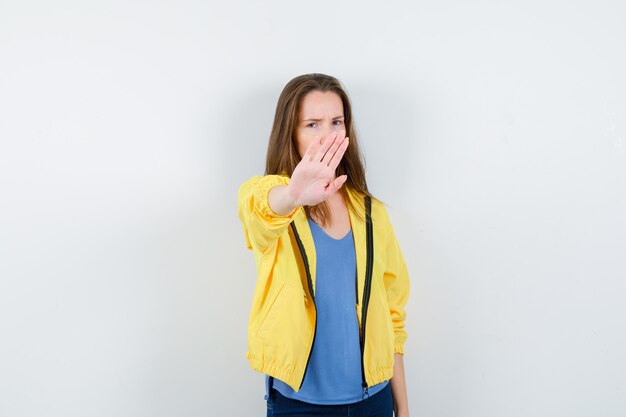 Junge Frau im T-Shirt, Jacke, die Stoppgeste zeigt und genervt aussieht, Vorderansicht.