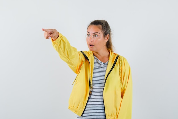 Kostenloses Foto junge frau im t-shirt, jacke zeigt weg und schaut erstaunt, vorderansicht.