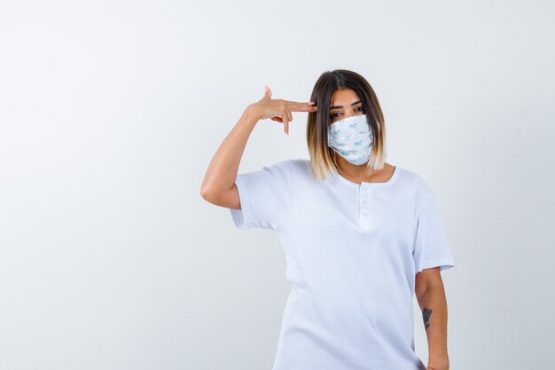 Junge Frau im T-Shirt, Maske, die Selbstmordgeste macht und hoffnungslos schaut, Vorderansicht.