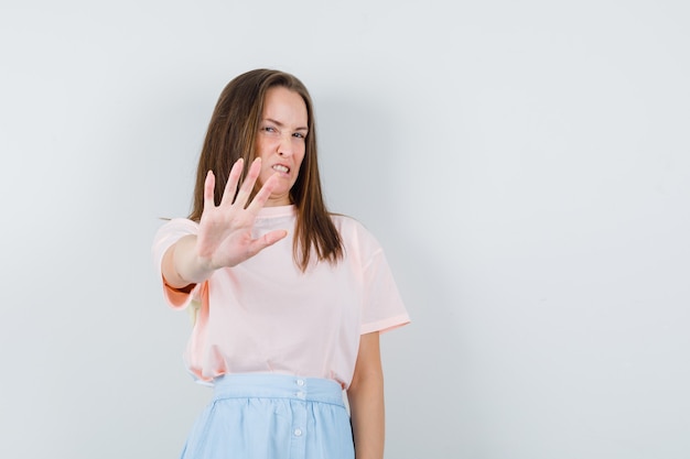 Junge Frau im T-Shirt, Rock, der Ablehnungsgeste zeigt und gereizt aussieht, Vorderansicht.