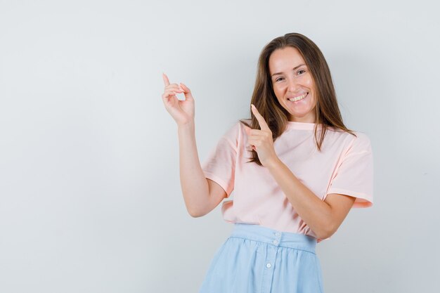 Junge Frau im T-Shirt, Rock zeigt nach oben und schaut fröhlich, Vorderansicht.