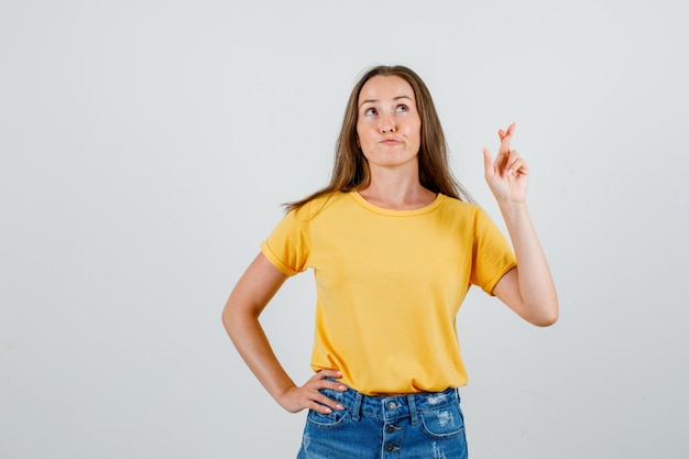 Junge Frau im T-Shirt, Shorts, die Finger kreuzen, während sie aufschauen und hoffnungsvoll aussehen