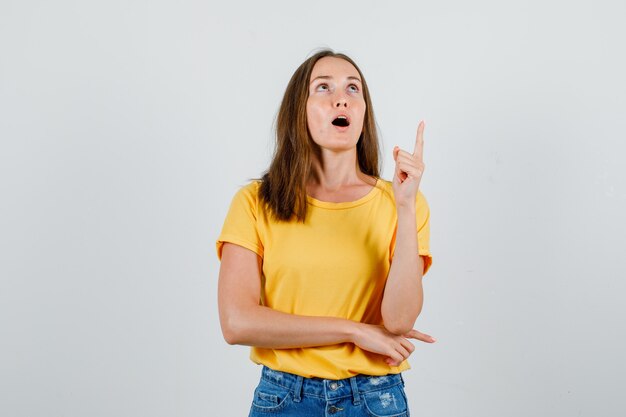 Junge Frau im T-Shirt, Shorts, die Finger nach oben zeigen und konzentriert schauen