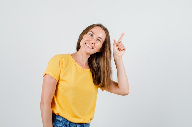 Junge Frau im T-Shirt, Shorts, die mit dem Finger nach oben schauen und fröhlich schauen