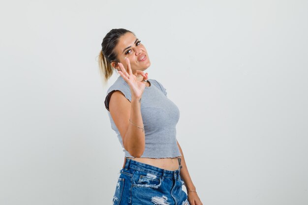 Junge Frau im T-Shirt, Shorts, die ok Zeichen zeigen und selbstbewusst aussehen
