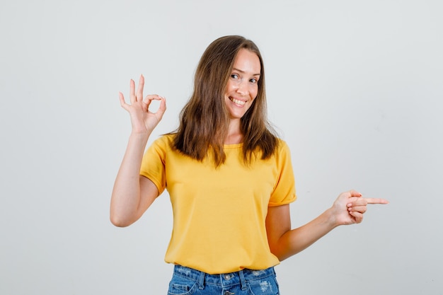 Junge Frau im T-Shirt, Shorts, die ok Zeichen zeigen, während sie weg zeigen und fröhlich aussehen