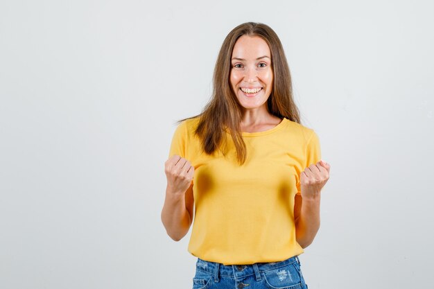 Junge Frau im T-Shirt, Shorts, die Siegergeste zeigen und fröhlich schauen