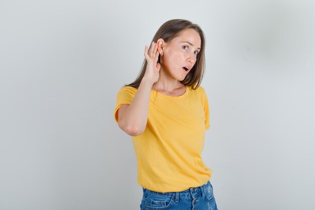 Junge Frau im T-Shirt, Shorts, die versuchen, Geheimnis zu hören und konzentriert aussehen