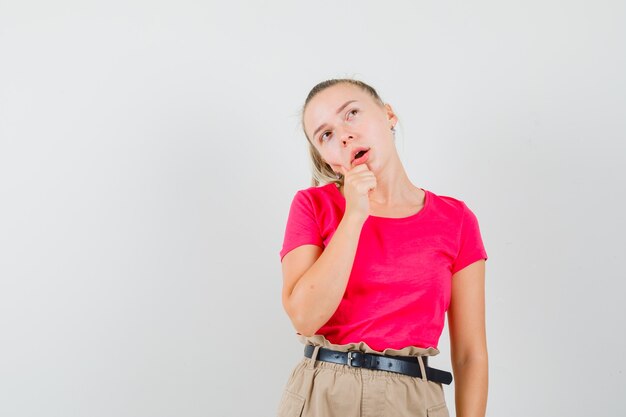 Junge Frau im T-Shirt und in der Hose, die ihr Kinn halten und verträumt aussehen