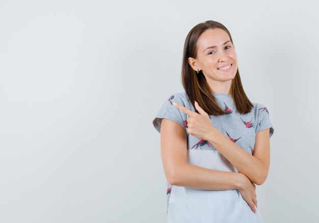 Junge Frau im T-Shirt zeigt weg und schaut zuversichtlich, Vorderansicht.